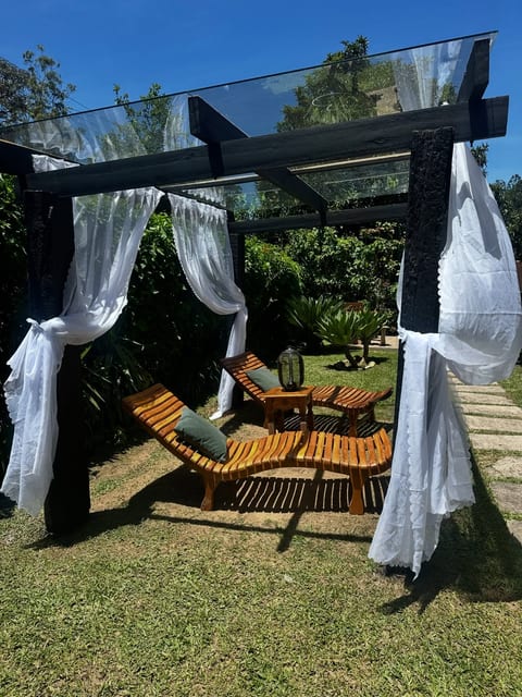 Espreguiçadeiras de madeira sob o gazebo de cortinas brancas no jardim da Pousada do Figa